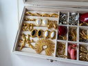 A collection of gold jewelry featuring fine jewelry designs with pearl accents and a sunburst gold art piece.