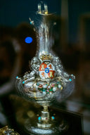 An ornate silver vase with gold accents, turquoise gemstones, and a royal crest featuring red and white shields in fine art gold jewelry.