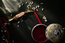 A decorative rakhi with pinkish-golden centerpiece and yellow beads on red thread inspired by famous cursed gems like hope diamond.
