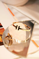 Gold-toned 18k gold fine jewelry bangle with sleek minimalist black t logo for jewelry investment appraisal.