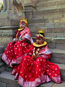 Two young girls wearing vibrant red garments with intricate gold jewelry and ornate golden headpieces inspired by cleopatric gold art gold