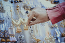 Hand in pink jacket touches ornate gold jewelry jhumka earring