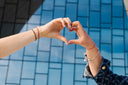 Two hands forming a heart shape against glass building