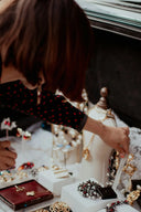 A woman in a black polka-dot top reaches for an ornate 18k gold fine jewelry necklace with pearls on display.