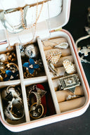 A white velvet-lined jewelry organizer with pink trim neatly holding art gold jewelry including rings and necklaces
