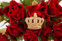 Glittery gold crown pin with cursed gems amid red roses