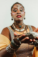 A woman wearing fine jewelry with turquoise beads and a silver headband holds a rough gray stone in her hands.