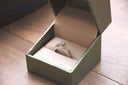 A delicate silver engagement ring with central and smaller diamonds in a green box highlighting luxury jewelry trends.
