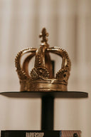 Golden ornate crown jewel in art gold with cross atop on black stand