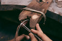 A silver-toned diamond-encrusted fine jewelry bracelet being meticulously crafted on a wooden workbench for art gold jewelry care