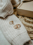 Two gold-toned fine jewelry rings with delicate diamond accents displayed on a cream-colored knitted sweater.
