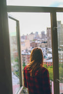 A woman in a red and black plaid shirt stands by an open window showcasing unique craftsmanship in luxury jewelry.