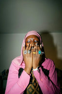 A person wearing a pink hijab and matching jacket adorned with fine 18k gold jewelry rings symbolizing meaning wrapped in metal