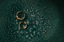 Two gold rings on a textured teal surface