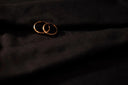 Two interlocking gold rings on dark fabric showcasing fine jewelry and versatile gold jewelry for men.
