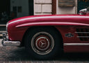 A glossy red mercedes-benz 300 sl with chrome accents and wire-spoke wheels inspired by art gold jewelry craftsmanship