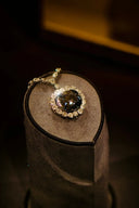 A dark faceted gemstone pendant in fine art gold jewelry with a diamond halo on an ornate gold chain