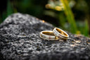 Two gold wedding bands featuring a subtle diamond band and a smooth design on a dark textured rock for fine jewelry.