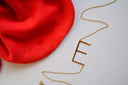 A red satin bag and a gold necklace on a white surface