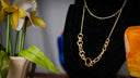 a gold necklace on a mannequin next to a vase with flowers