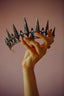 a hand holding a tiara in front of a pink background