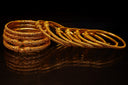 A stack of ornate gold bangles on a dark surface.