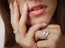 Woman's hand wearing diamond rings near her face