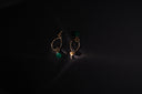 Gold earrings with green beads on black background