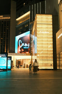 People walking past illuminated stores at night.