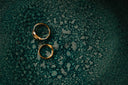Two gold rings on a textured teal surface