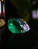 A rough, uncut emerald gemstone with vibrant green hues.