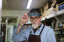Man with magnifying glasses adjusts headband in workshop.