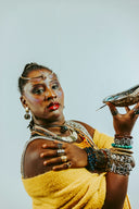Woman adorned with elaborate jewelry and face paint holds shell.