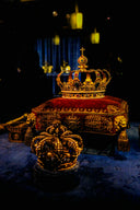 Two ornate golden crowns displayed on velvet cushions