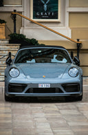 A grey porsche convertible parked in front of a building.