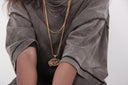 Person in grey t-shirt with multiple gold chain necklaces.