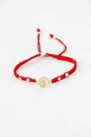 A red string bracelet with a gold medallion and beads