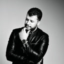 A man in a leather jacket looking down thoughtfully.