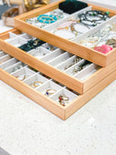 Stacked bamboo jewelry trays with compartments containing various rings, bracelets, and necklaces