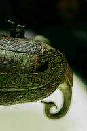 A close-up of an ancient bronze vessel with intricate scale and scroll patterns.