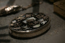 An oval silver box with black inlay and mother of pearl floral patterns