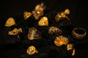 A collection of ornate gold rings resting on dark charcoal pieces