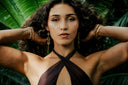 A woman with curly hair and gold jewelry against a background of palm fronds