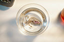 A silver chain necklace with a pink oval pendant submerged in a glass