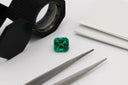 A vibrant emerald-cut green gemstone examined with tools on a white surface for rare engagement rings at everett jewelry store