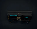 Gold-rimmed Cartier glasses with dark teal lenses rest on black leather case in Roberto Coin versus Pomellato fine jewelry article.