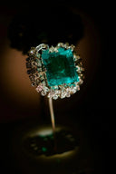 A radiant emerald-cut green engagement ring with diamond halo set in an intricate platinum art gold jewelry band.
