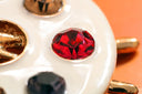 A glossy white ceramic palette featuring a red faceted rhinestone and 18k gold accents inspired by famous cursed gems