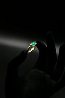 a person's hand holding a ring with a green stone