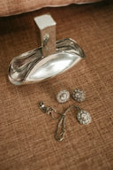 a pair of silver earrings sitting on top of a bed